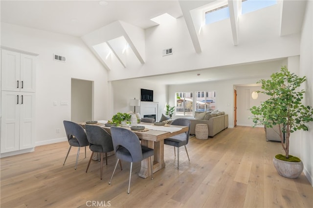 dining area featuring light hardwood / wood-style flooring, high vaulted ceiling, and a skylight