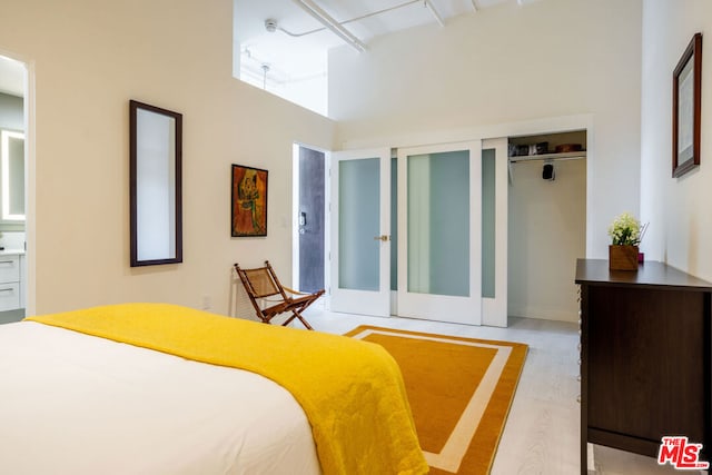 bedroom with french doors, a towering ceiling, light hardwood / wood-style floors, and a closet