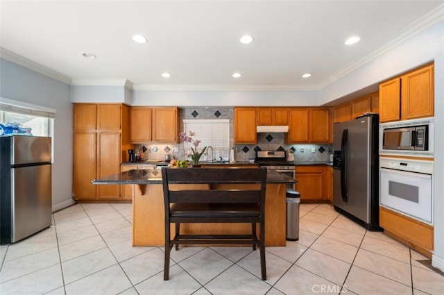 kitchen with a kitchen island, crown molding, appliances with stainless steel finishes, a breakfast bar area, and dark stone counters