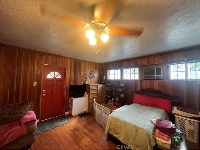 bedroom with ceiling fan, wood-type flooring, wooden walls, and a textured ceiling