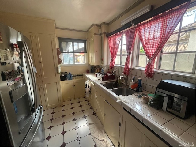 kitchen featuring cream cabinetry, stainless steel fridge, tile counters, crown molding, and sink