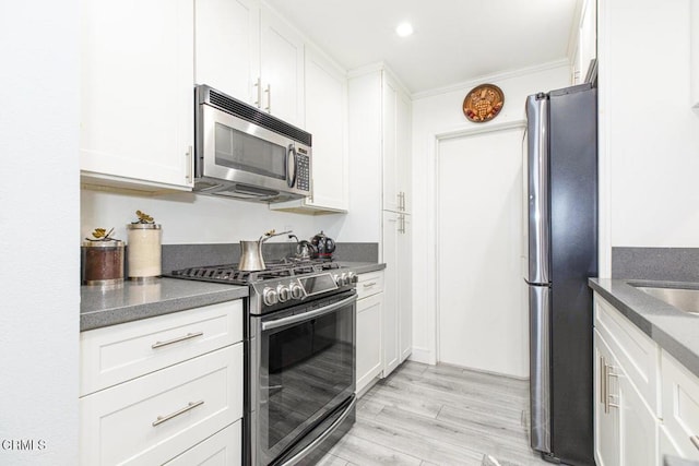 kitchen featuring white cabinetry, crown molding, stainless steel appliances, and light wood-type flooring