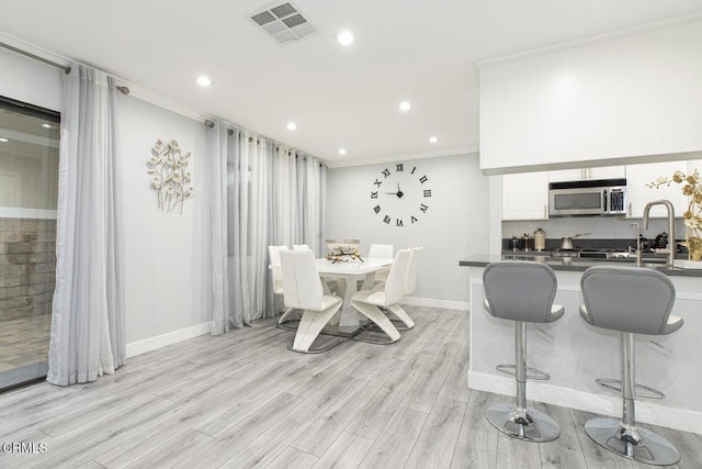 dining space with sink, light hardwood / wood-style flooring, and ornamental molding