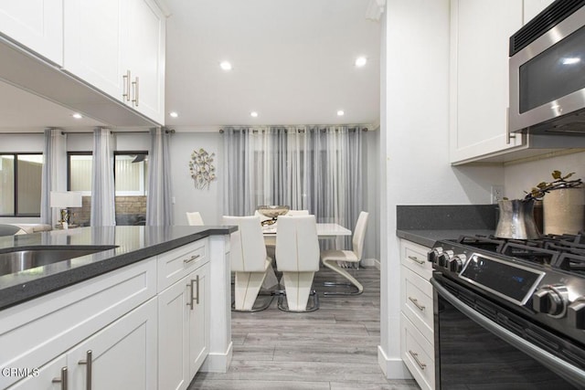 kitchen featuring white cabinets, black gas stove, light hardwood / wood-style flooring, and dark stone counters