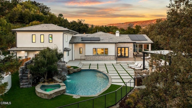 back house at dusk with a swimming pool with hot tub, pool water feature, a patio area, and a lawn