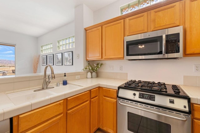 kitchen with tile counters, plenty of natural light, sink, and stainless steel appliances