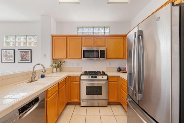 kitchen with tile counters, sink, light tile patterned floors, and appliances with stainless steel finishes