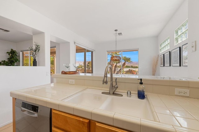 kitchen with tile counters, stainless steel dishwasher, decorative light fixtures, and sink