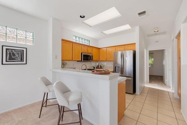 kitchen with kitchen peninsula, appliances with stainless steel finishes, a kitchen bar, and light tile patterned floors