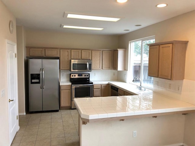 kitchen with kitchen peninsula, appliances with stainless steel finishes, decorative backsplash, tile counters, and light tile patterned flooring