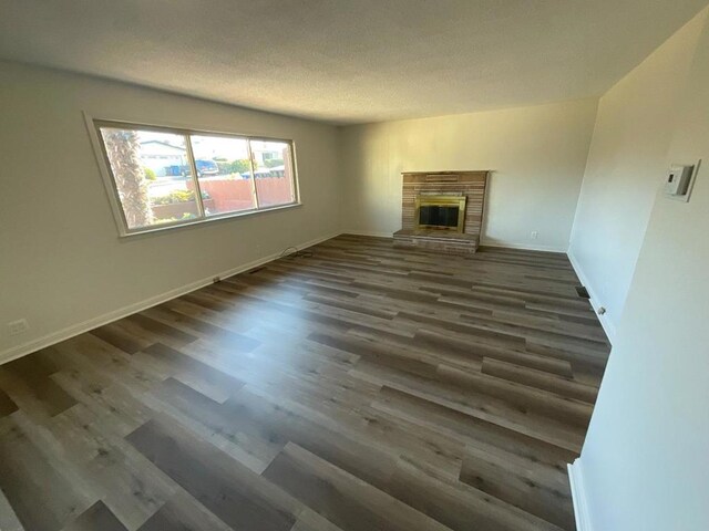 unfurnished living room featuring a textured ceiling, dark wood-type flooring, and a brick fireplace