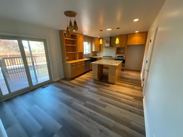 kitchen with wall chimney exhaust hood, decorative light fixtures, hardwood / wood-style flooring, a kitchen island, and appliances with stainless steel finishes