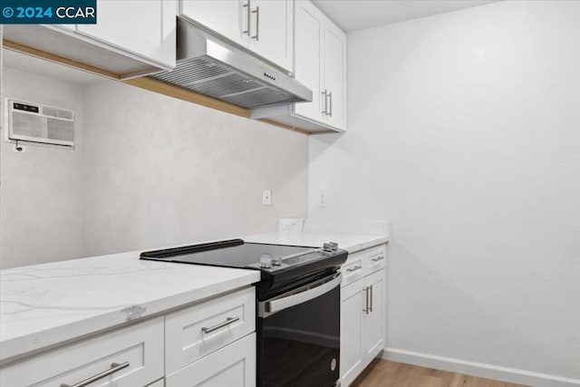 kitchen with a wall unit AC, white cabinetry, light hardwood / wood-style flooring, and black electric range oven