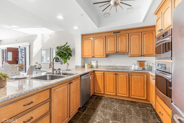 kitchen with a raised ceiling, sink, ceiling fan, light stone countertops, and stainless steel appliances