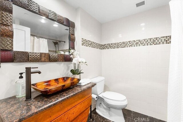 bathroom featuring vanity, tile patterned flooring, a shower with shower curtain, toilet, and tile walls