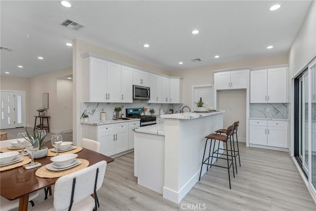 kitchen with light wood-type flooring, white cabinetry, an island with sink, and appliances with stainless steel finishes