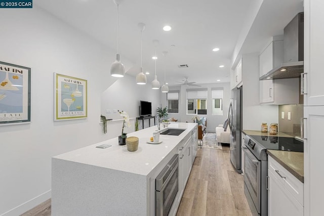 kitchen with appliances with stainless steel finishes, wall chimney exhaust hood, a kitchen island with sink, pendant lighting, and white cabinets