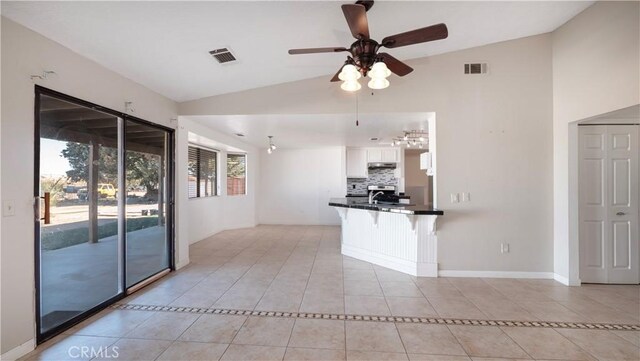 kitchen featuring light tile patterned flooring, lofted ceiling, white cabinets, a kitchen bar, and kitchen peninsula