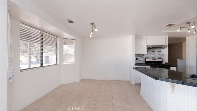 kitchen with white cabinets, light tile patterned floors, stainless steel range, and decorative backsplash