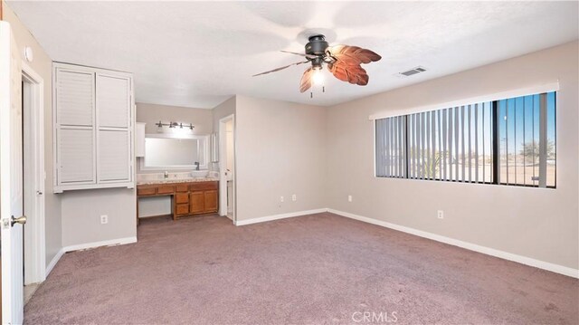 unfurnished bedroom with ceiling fan, ensuite bathroom, built in desk, and carpet