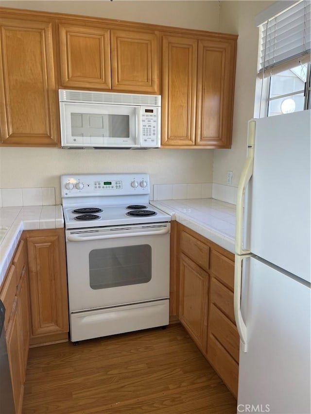 kitchen with tile counters, white appliances, and hardwood / wood-style flooring