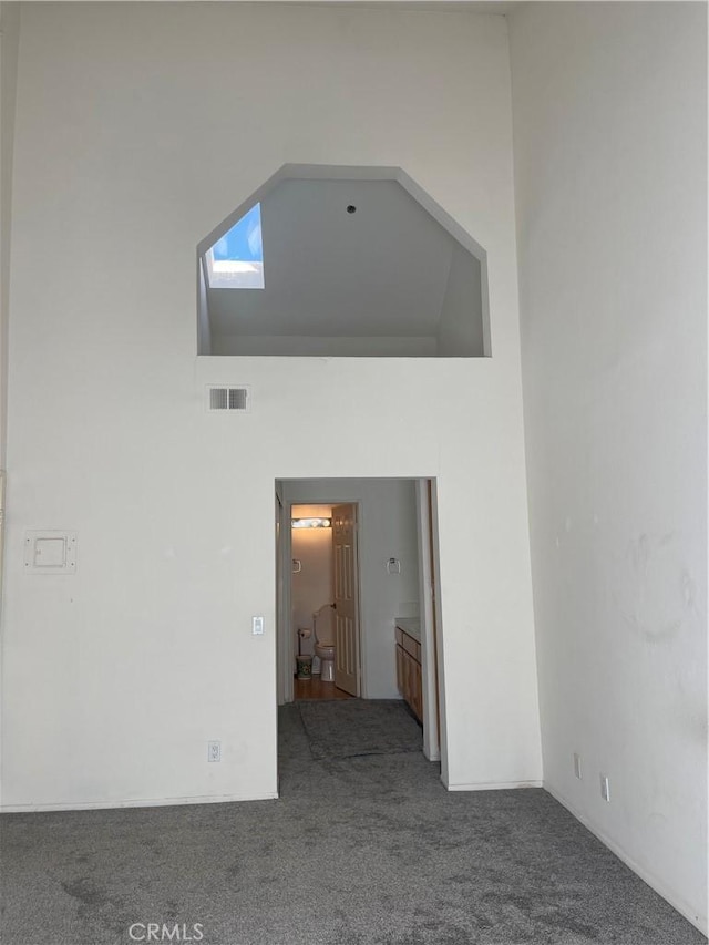 empty room with carpet, a high ceiling, and a skylight