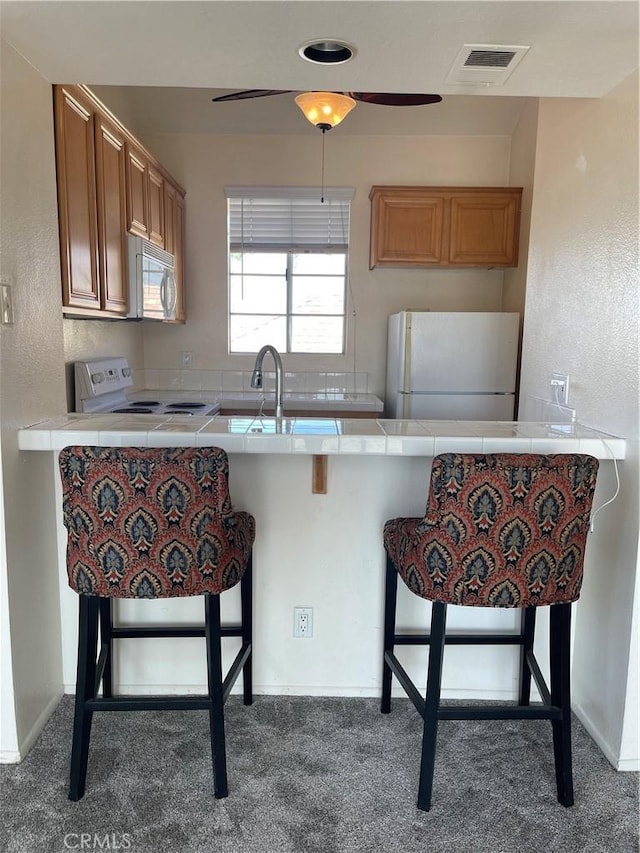 kitchen featuring carpet flooring, white appliances, kitchen peninsula, and a breakfast bar area