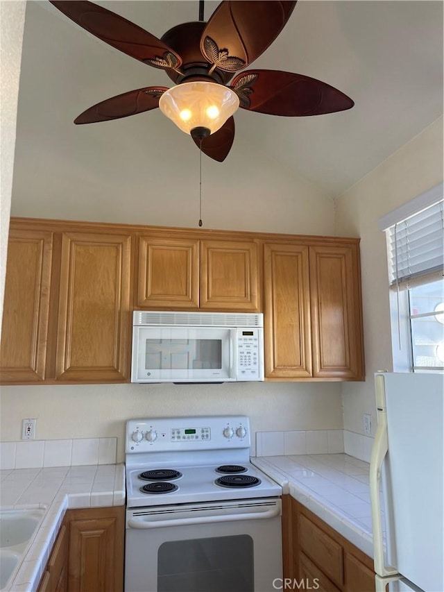 kitchen with ceiling fan, tile counters, sink, vaulted ceiling, and white appliances