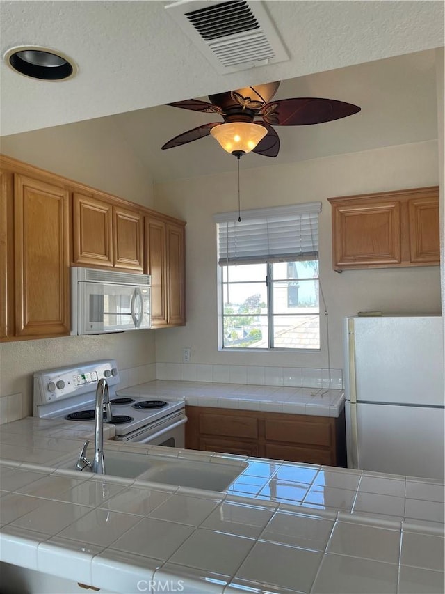 kitchen featuring lofted ceiling, tile counters, ceiling fan, and white appliances