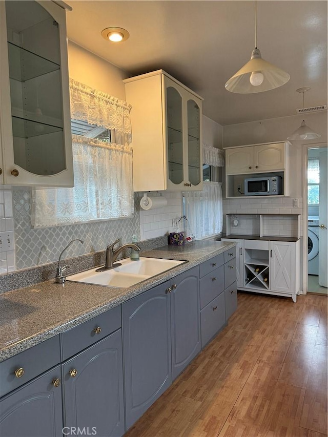 kitchen with backsplash, sink, light hardwood / wood-style flooring, washer / clothes dryer, and hanging light fixtures