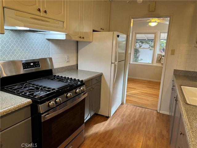 kitchen with white fridge, stainless steel gas range oven, light hardwood / wood-style floors, and backsplash