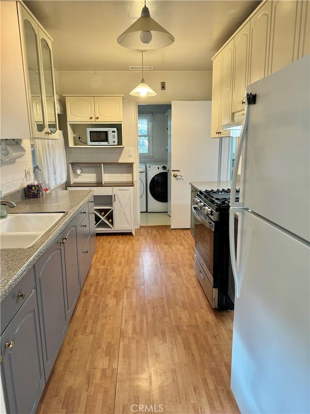 kitchen featuring white cabinetry, sink, separate washer and dryer, decorative light fixtures, and white appliances