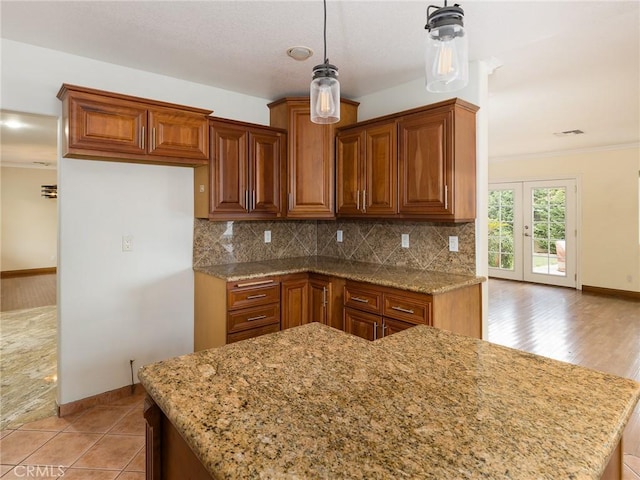 kitchen with tasteful backsplash, crown molding, light stone countertops, and decorative light fixtures