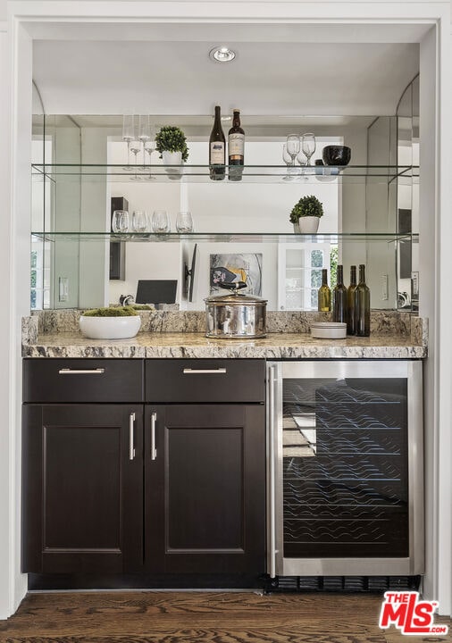 bar with dark brown cabinetry, light stone countertops, sink, wine cooler, and dark hardwood / wood-style floors