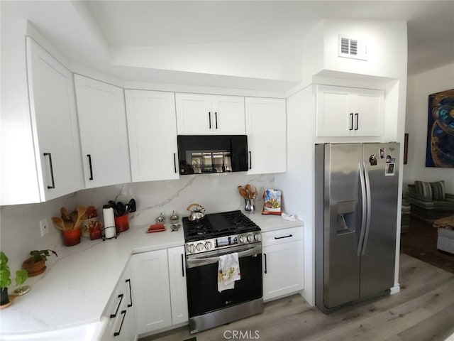 kitchen with white cabinetry, stainless steel appliances, vaulted ceiling, and light wood-type flooring