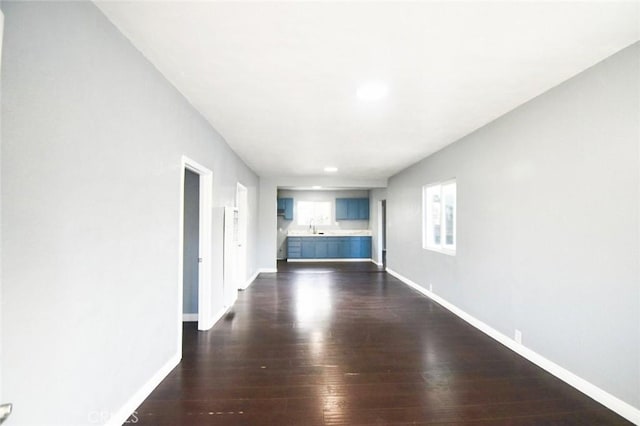 unfurnished living room featuring a sink, baseboards, and dark wood-type flooring