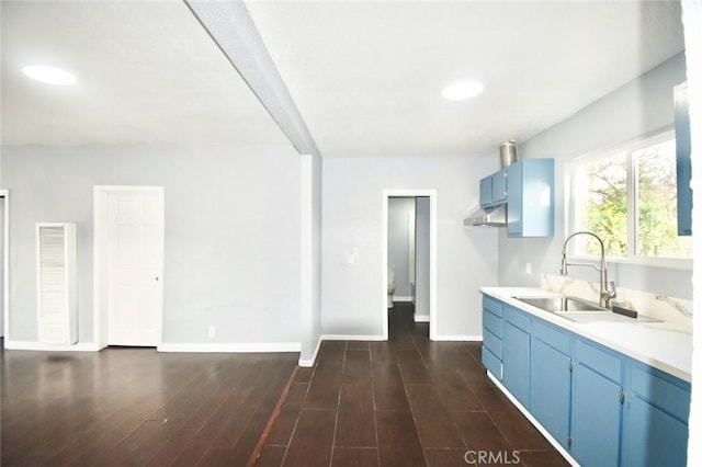 kitchen featuring blue cabinetry, light countertops, dark wood-type flooring, a sink, and under cabinet range hood