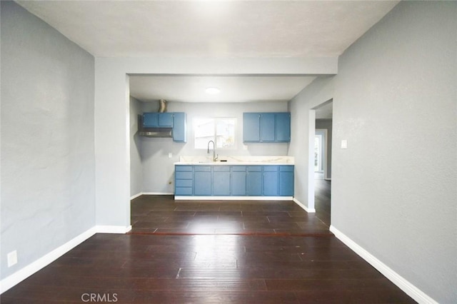 kitchen featuring dark wood finished floors, blue cabinetry, light countertops, a sink, and baseboards