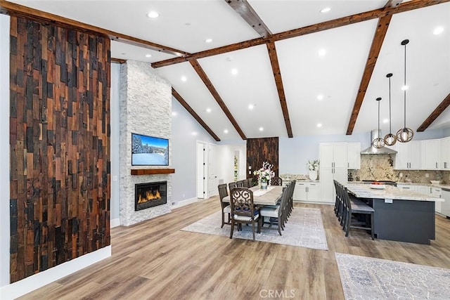 dining room with beam ceiling, light wood-type flooring, and a stone fireplace