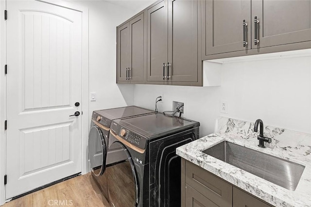 washroom with washing machine and dryer, sink, cabinets, and light wood-type flooring