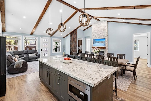 kitchen featuring stainless steel microwave, decorative light fixtures, a breakfast bar area, a kitchen island, and light wood-type flooring