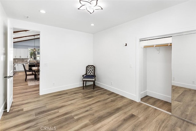 unfurnished bedroom featuring beam ceiling, a closet, and hardwood / wood-style flooring