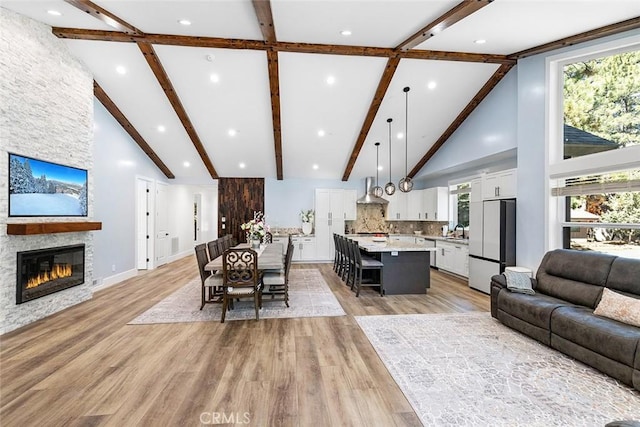 living room featuring a stone fireplace, beamed ceiling, high vaulted ceiling, and light wood-type flooring