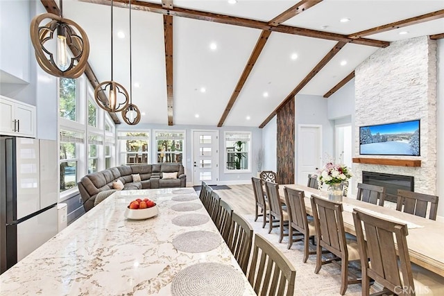 dining area featuring an inviting chandelier, light hardwood / wood-style flooring, high vaulted ceiling, beamed ceiling, and a stone fireplace