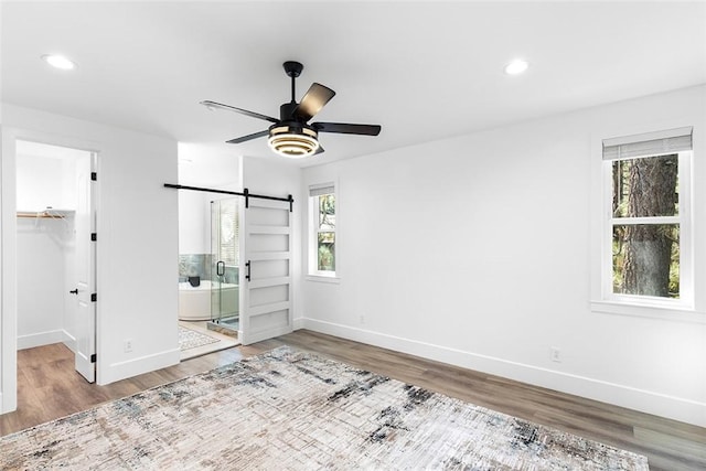 unfurnished bedroom with multiple windows, a barn door, ensuite bathroom, and ceiling fan