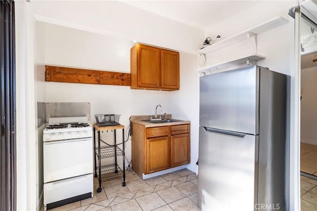 kitchen featuring stainless steel fridge, light tile patterned floors, sink, and gas range gas stove