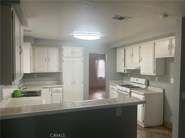 kitchen featuring kitchen peninsula, white gas range, white cabinetry, and tile counters