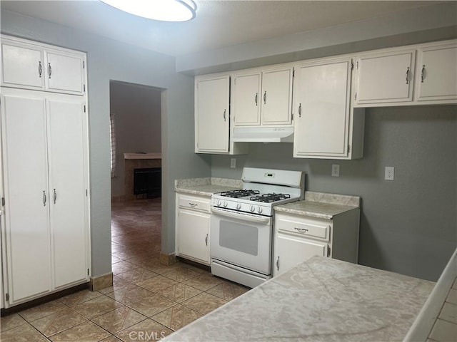 kitchen featuring white range with gas stovetop, light tile patterned floors, white cabinetry, and a fireplace