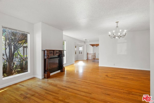 unfurnished living room featuring plenty of natural light, an inviting chandelier, a textured ceiling, and light hardwood / wood-style floors