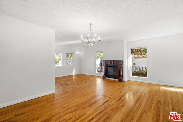 unfurnished living room featuring a textured ceiling, an inviting chandelier, and light hardwood / wood-style flooring